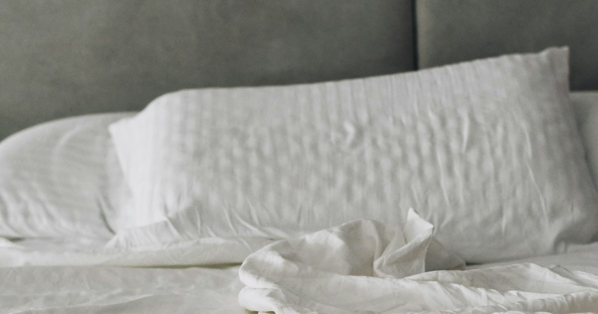 Bed made with white cotton sheets and pillowcases against a grey upholstered headboard